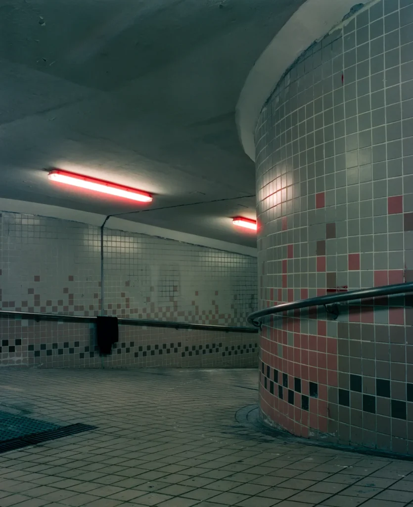 붉은 조명 아래 노출된 옛 대중목욕탕의 곡선형 모자이크 타일 벽면과 핸드레일의 모습으로, 공간의 건축적 특징과 생활사를 기록한 아카이브 사진